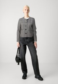 Svart-hvitt houndstooth-jakke med lange ermer og rund hals, med knappelukking, kombinert med høytlivde svarte jeans og joggesko.
