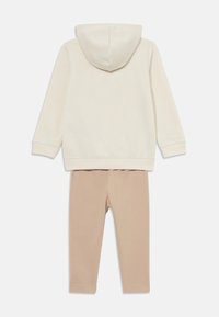 Krämfärgad hoodie med en framficka i känguru-stil och beige leggings i mjukt tyg, med en enkel, odekorerad design och figurnära passform.