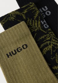 Vihreä ribbineulottu sukka, jossa "HUGO"-logo, musta sukka vihreällä kuviolla, ja yksivärinen musta sukka, jossa harmaa "HUGO"-logo. Puuvillasekoitemateriaaleja.