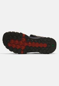 Shoe outsole features a rugged black rubber design with red and green accents, showcasing deep treads for traction and stability.