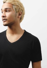 Czarny t-shirt z dekoltem w serek i krótkimi rękawami, wykonany z gładkiego materiału. Model ma jasne, falowane włosy i krótko ostrzyżoną brodę.