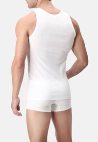 Canotta bianca realizzata in morbido cotone. Design aderente con spalline larghe, texture liscia, abbinata a pantaloni boxer bianchi.