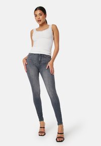 Vit ribbad linne med spetsdetalj vid nacklinjen, tillsammans med mörkgrå skinny jeans. Modellen står i öppna svarta klacksandaler.