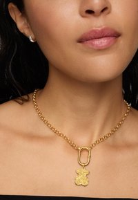 Collar de cadena de oro con grandes eslabones circulares y un colgante de oso de oro, con un acabado texturizado que resalta contra la piel.