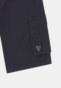 Crne cargo kratke hlače izrađene od mješavine pamuka; imaju bočnu džepu i trokutasti logotip na prednjoj strani. Glatka tekstura i ležeran dizajn.