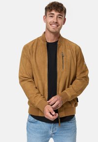 Brown suede bomber jacket with ribbed cuffs and hem, featuring a zippered chest pocket and zip front closure, worn over a black t-shirt.