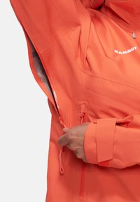 Orange vandtæt jakke med lynlåsåbning, justerbare manchetter og struktureret stof. Har branding og elastiske snore.