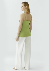 Grünes, tailliertes Tanktop mit verstellbaren Trägern, kombiniert mit weiten weißen Hosen. Das Material wirkt glatt, mit einem schlichten Design und minimalen Details.