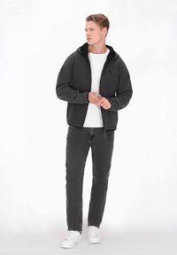 Grå fleece-hoodie med dragkedja, framfickor och en svart emblem. Kombinerad med urblekta svarta jeans och vita sneakers. Enkel, avslappnad design.