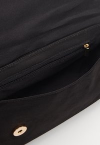 Vnitřek černé látkové tašky s kapsou na zip, ozdobený zlatým kovovým cvokem a texturovaným podšíváním.