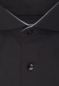 Schwarz hochgeschlossenes Hemd mit einem kontrastierenden weißen Kragenrand, mit einem schwarzen Knopf und glattem, strukturiertem Stoff.