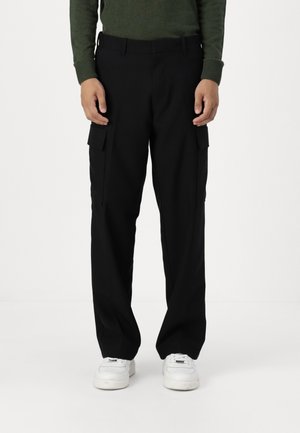 Pantaloni cargo negri cu un design drept, dotati cu buzunare laterale, o textură netedă și o talie ajustată. Purtați cu adidași albi.