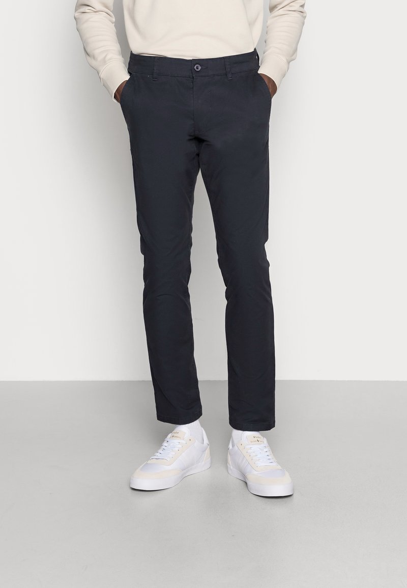 Chinos bleu marine à coupe slim, fabriqués en tissu mélangé coton. Comprend des poches avant, une fermeture à un bouton et des ourlets retroussés. Portés avec des baskets blanches.