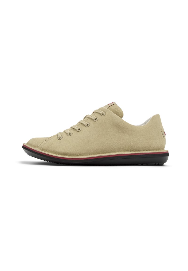 Sneaker in suede beige con sei asole, superficie tessurizzata, bordo rosso a contrasto lungo la suola e suola in gomma nera.