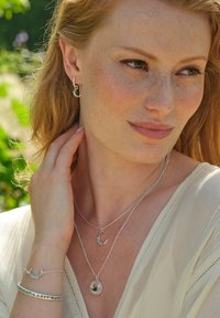 Las joyas de plata incluyen collares en capas con acentos de luna creciente, un colgante circular y pendientes a juego de aro. Una pulsera floral completa el look.