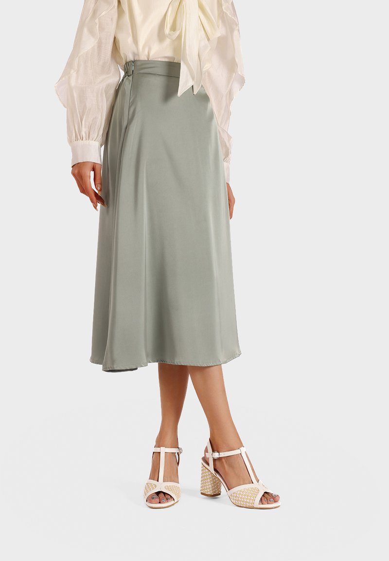 Gonna in satin verde chiaro con una silhouette morbida e cerniera laterale, abbinata a sandali con tacco alto in bianco e beige con cinturini intrecciati.