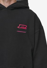 Felpa nera con cappuccio caratterizzata da un logo grafico rosa e un'etichetta. Realizzata in misto cotone con finitura strutturata. Design con cappuccio e tasca a marsupio.