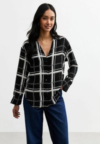 Camicia a maniche lunghe bianca e nera con motivo a catena e dettagli con bottoni, caratterizzata da un scollo a V e una vestibilità rilassata.