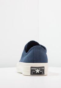 Baskets basses en toile bleu marine avec semelle en caoutchouc blanche et étiquette noire brillante affichant un texte blanc et un logo étoile sur le talon.