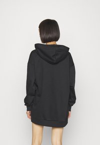 Sudadera negra con capucha, de corte holgado, mangas largas y aberturas laterales, hecha de un tejido suave y texturizado, con un diseño sencillo.