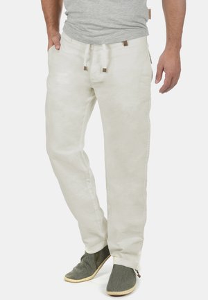 Vita linbyxor med avslappnad passform, med justerbart snörmidja och sidofickor, kombinerade med strukturerade gröna slip-on skor.