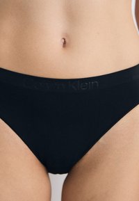 Crni Calvin Klein donji veš prikazan je na neutralnoj pozadini, ističući logo na pojasu i glatku teksturu tkanine.