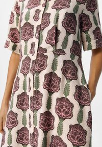 Robes à boutons floraux en tissu léger, présentant un motif de fleurs roses reproduites, des feuilles vertes et des manches courtes.