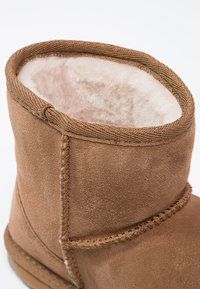 Brązowe zamszowe botki z miękkim, białym futerkiem w środku. Posiadają przeszycia i zaokrąglony górny fason. Gładka struktura.