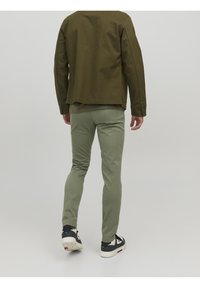 Olivgrön jacka med en avslappnad passform, tillverkad av bomull, och långa ärmar. Matchad med smalt skurna, ljusgröna byxor och svarta sneakers.