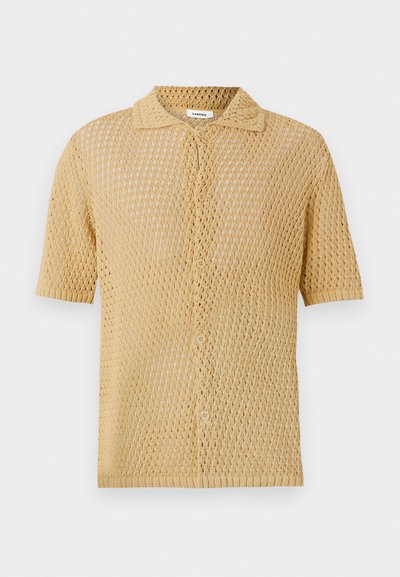 Kortermet, knappet skjorte i lys beige. Har et løst, åpent strikk med et teksturert mønster og en standard krage.