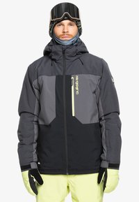 Herren Schneejacke in Grau und Schwarz, ausgestattet mit einer Reißverschluss-Brusttasche und einer verstellbaren Kapuze, ergänzt durch beleuchtete Akzente. Strukturierter Stoff und Bündchen.