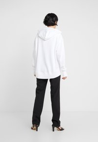 Felpa bianca con cappuccio a coulisse, vestibilità rilassata e polsini a costine, abbinata a pantaloni neri su misura e sandali neri con tacco alto.