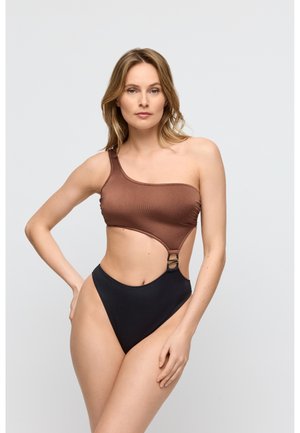 Einteiliger Badeanzug mit braunem, geripptem Oberteil und asymmetrischem Schnitt sowie schwarzem, hoch-tailliertem Unterteil, akzentuiert durch einen goldfarbenen Ring an der Seite.