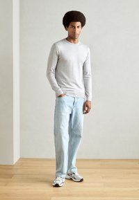 Light gray long-sleeve shirt, blue loose-fitting jeans, and white sneakers with black accents. Simple, clean lines; cotton material.
