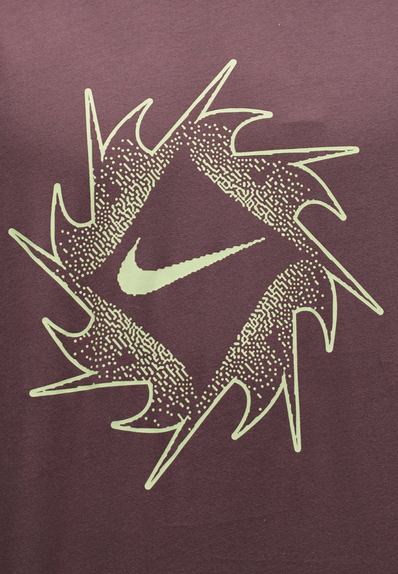 Nike-Logo zentriert in einer gezackten Diamantform mit gepunkteten und strukturierten Mustern auf einem weinroten Stoffhintergrund.