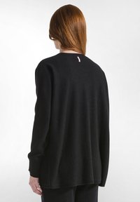 Maglione nero oversize realizzato in tessuto morbido, con colletto tondo e un piccolo dettaglio rosa sul retro. Maniche lunghe e vestibilità comoda.