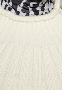 Kermitt värvitud kootud sviiter ribitud tekstuuri ja kõrge kraega. Kaela ümber on nähtav must-valge mustriga sall.