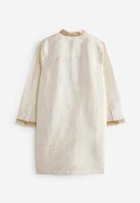 Chemise traditionnelle longue de couleur crème avec bordure dorée au col et aux poignets, vue de dos sur fond blanc.