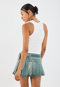 White fitted tank top paired with a pleated denim mini skirt, featuring light blue hues and a faded texture, with visible stitching details.