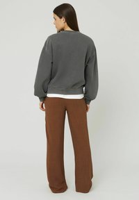 Sweatshirt gris avec des manches bouffantes et un ourlet côtelé, associé à un pantalon large marron. Texture lisse et coupe décontractée.