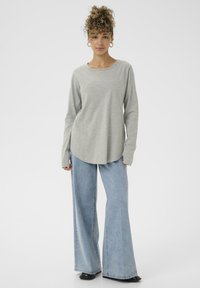 Lys grå langærmet top med rund hals, parret med brede lette blå denimbukser. Glat stof og afslappet pasform.