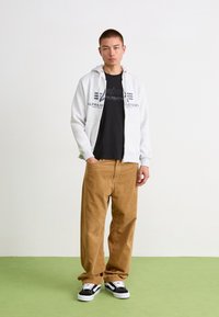 Grijze zip-up hoodie met logo, zwarte T-shirt, tan corduroy broek en zwarte sneakers. Glad textuur en ontspannen pasvorm overal.