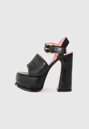 Black leather platform high heel sandal with wide strap, ankle buckle, and thick block heel, shown on a plain light background.