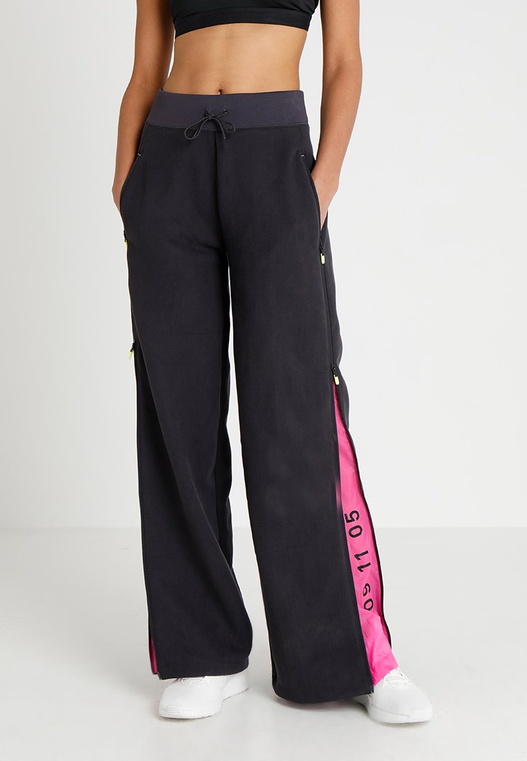 Pantalons larges noirs avec des panneaux latéraux roses comportant des poches zippées. Taille à cordon, fabriqués dans un tissu lisse avec une coupe décontractée.