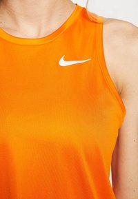 Haut de sport sans manches orange avec une texture lisse, arborant un logo Nike blanc sur le côté gauche de la poitrine et un col rond.