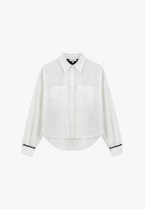 Blusa blanca corta en tela ligera. Presenta un cuello clásico, cierre de botones, dos bolsillos en el pecho y detalles en negro en los puños.