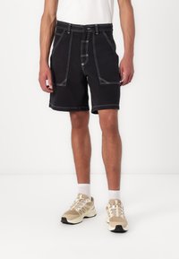 Svarte shorts med hvit søm og høy midje. Har to frontlommer og beltehemper. Kombinert med beige sportsko.