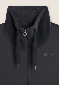 Giacca sportiva grigia scura con colletto in morbido fleece, zip frontale e coulisse; presenta il logo "FREDDY" con accenti di borchie.