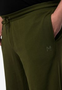 Olijfgroene joggers met een trekkoord in de taille en zijzakken. Voorzien van een subtiele logo op de linker dij. Zacht, lichtgewicht stof.