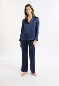 Granatowy satynowy komplet piżamowy z bluzką na guziki i luźnymi spodniami. Posiada długie rękawy i kołnierz z wycięciem. Gładka faktura.